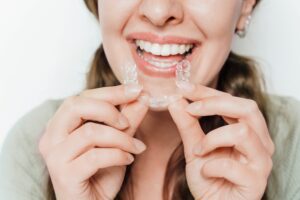 young woman smiling and putting in her clear aligners against a white background